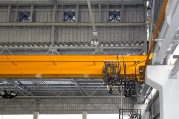 Fototapeta premium Overhead crane in factory or warehouse. Industrial machine or lifting equipment with hoist, hook and wire rope on beam girder structure. Include ventilation fan at side wall for cool, air flow.