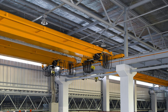 Overhead crane inside factory or warehouse building. Industrial machine or lifting equipment consist of hoist, hook and wire rope move on beam girder structure for manufacturing production plant.