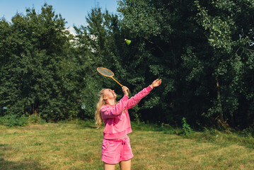 Pretty young woman play with Neon yellow badminton shuttlecock and racket on green grass outdoors....