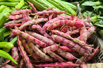 Close-up of fresh cranberry beans "also known as borlotti beans" in their vibrant pink and speckled pods at a traditional wet market vegetable stall.
