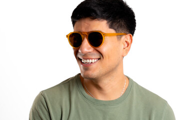 Young smiling Latin man, wearing sunglasses, looks away on white background