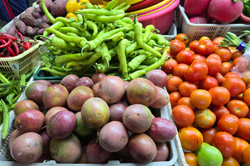 A vibrant market display with green chilies, tomatoes, passion fruits, and other fresh produce in baskets.
