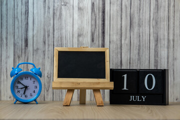 Blank black board for chalk notes mock up template for your design write your to-do list and a wooden calendar with the date July 10 on the table set against alarm clock and wooden background
