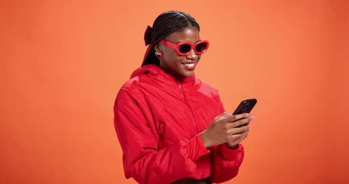 Woman, sunglasses and thinking with phone in studio for text solution, response idea or aha moment. Mockup, fashion and black person with smartphone for social media inspiration on orange background