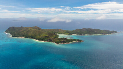 A scenic aerial view of a tropical island with turquoise waters surrounding white sandy beaches and lush greenery. Curieuse, Seychelles.