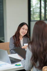 Two Asian businesswomen are sitting in a meeting, planning investment plans, business strategies. On the table are documents and graphs.
