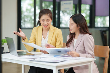 Two Asian businesswomen are sitting in a meeting, planning investment plans, business strategies. On the table are documents and graphs.