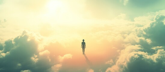 Solitary figure walking on clouds towards bright sun.