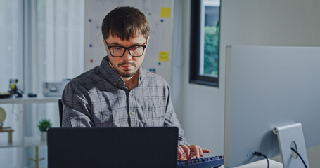 Young adult male freelance developer typing write prompt AI bot app program nomad terminal with coding at office. Artificial intelligence dashboard, robotics, user interface, machine learning concept.