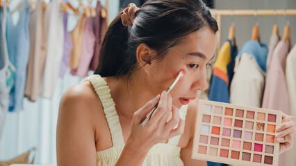 Young beautiful Asia lady blogger looking at camera recording swatch apply eyeshadow palette on skin show review to follower product vlog video live streaming at home. Business online media concept.