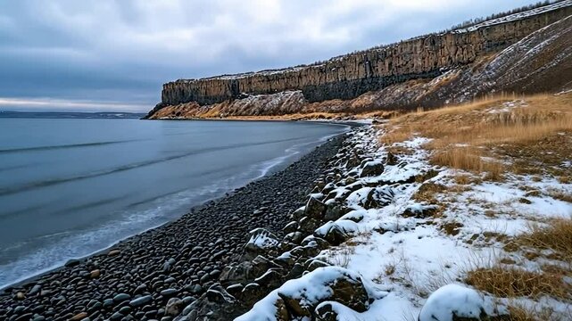 Coastal landscape of rocky beach and cliff under cloudy sky with snow patches