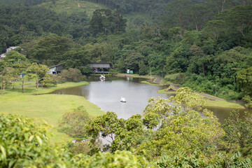 Obraz premium A serene small lake surrounded by lush greenery and rolling hills, with a peaceful boat floating at the center. A scenic nature view capturing the tranquility of a rural landscape