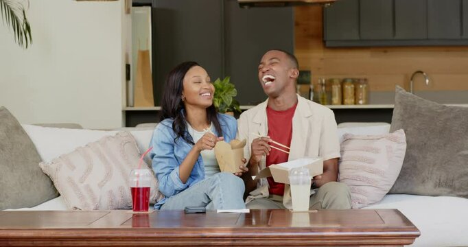 Greeting viewers, African American couple tasting takeout with chopsticks and sharing meal on sofa