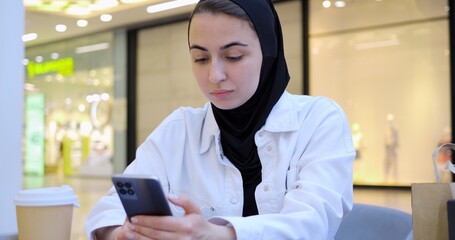 Young woman engaging with smartphone while enjoying coffee in trendy cafe, embodying modern digital connectivity and leisurely urban lifestyle during focused moment of communication