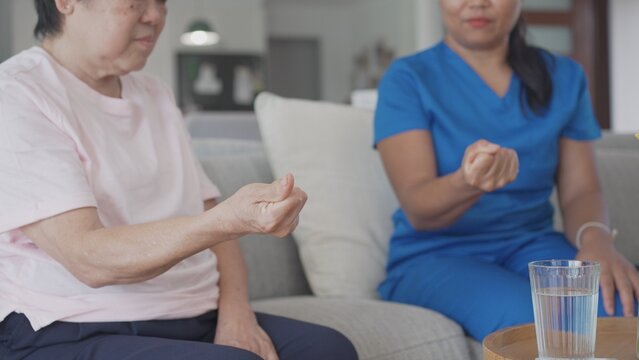 Asian health care worker giving elderly woman physiotherapy at home, home nurse, home care service concept