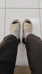 A pair of legs wearing black pants,  socks and brown sandals