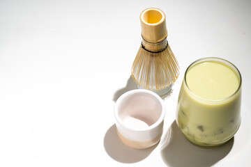 Closeup view of iced matcha green tea on the glass with a traditional bamboo brush whisk or chasen on a white background. Accessories for making matcha green tea
