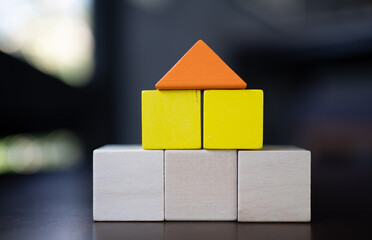 Colorful wooden building blocks stacked as house shape with orange triangle roof on yellow and...