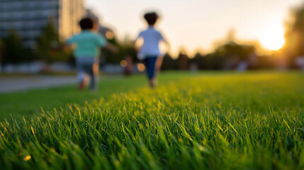 Obraz premium Two children running across green grass in city park at sunset. 