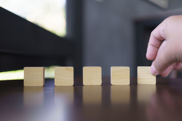 Hand placing wooden cube blocks in a row on reflective surface, business strategy concept, building...