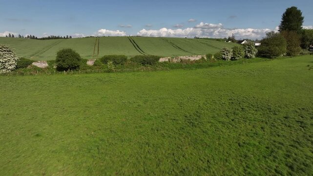 Caledon Border Wall, County Tyrone, Northern Ireland, May 2023. Drone push-in over green farmland, rolling fields, rural serenity and border visuals on sunny day under blue skies.