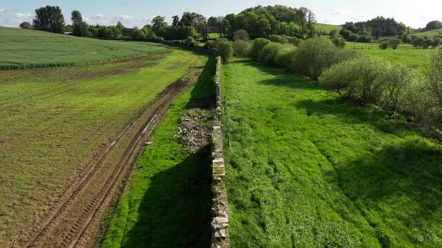 Caledon Border Wall, County Tyrone, Northern Ireland, May 2023. Drone moving forward over historic divide wall with scenic greenery, open fields and historic Irish countryside.