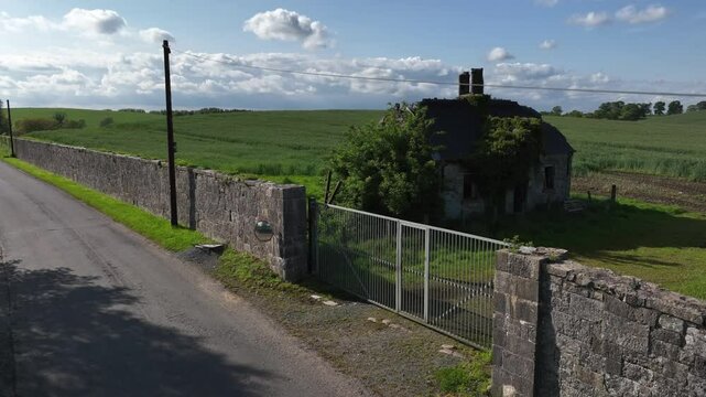 Caledon Border Wall, County Tyrone, Northern Ireland, May 2023. Drone slowly ascending, derelict house, historic divide wall and vast green farmland, rural decay and historic landscape beauty.