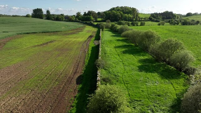 Caledon Border Wall, County Tyrone, Northern Ireland, May 2023. Drone slowly descends then glides forward over stone heritage, green fields, farmlands and scenic countryside in vibrant spring colors.