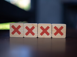 Four wooden blocks with red X marks in a row on reflective surface, business failure concept,...