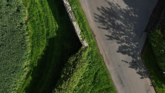Caledon Border Wall, County Tyrone, Northern Ireland, May 2023. Drone ascending twist, border wall, rural road and vibrant green fields, historic landscape aerial view on sunny day.