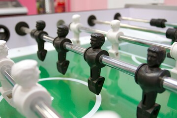 Black and white people playing on a table football field. Board sports game with black and white football players