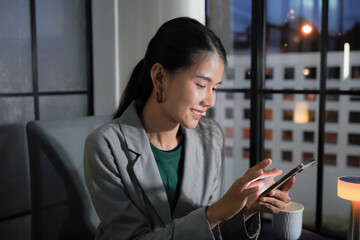 Asian businesswoman using smartphone checking e-mail during working at night time