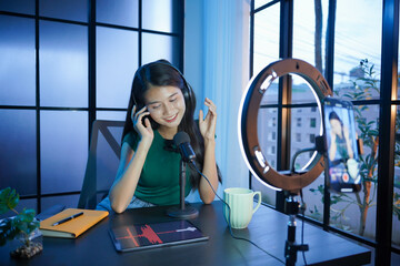 Asian woman in casual wearing headphones doing podcast in living room