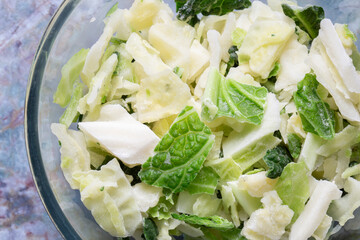 Frozen sliced cabbage defrosting in a glass bowl background backdrop. On a green marble background.