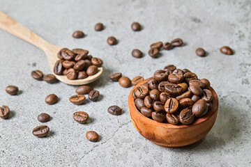 Close up view of coffee beans in the small or little wooden bowl. wooden spoon. grey or gray cement background. Scattered. nobody.