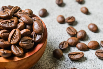 Extreme close up view of coffee beans in the small or little wooden bowl. grey or gray cement background. Scattered. nobody.