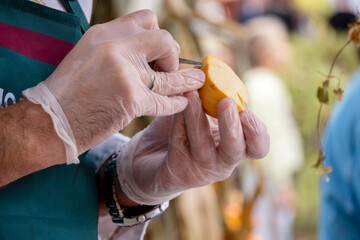 Close-up image of gloved hands intricately carving a design into an apple slice using a small...