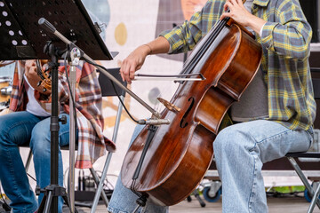 Musicians sitting on stage perform a live cello and violin duet, showcasing their musical talent. The players focus intently, adding a dynamic atmosphere to the performance.