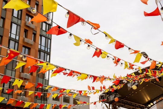 Vibrant orange, yellow, and red bunting lines strung with outdoor lights create a festive atmosphere against the backdrop of city buildings.