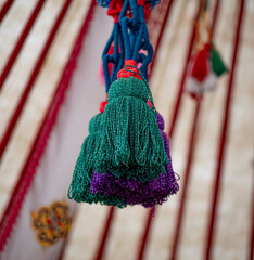 The photo shows a close-up of bright handmade wool pom-poms hanging on a green cord. They are used as decorative elements in traditional yurts.