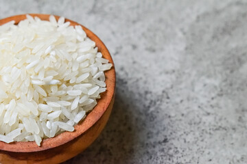 Extreme close up view of white raw rice in the little or small wooden bowl. Grey or gray cement on the background. Copy space, empty, free, negative.