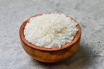 Close up view of white raw rice in the little or small wooden bowl. Grey or gray cement on the background.