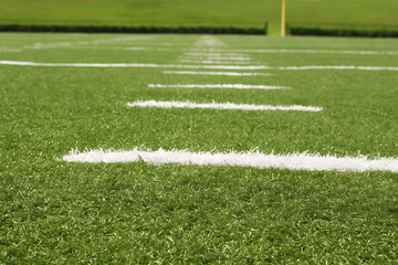 Obraz premium Close up of green artificial turf football field with white yard lines, goal post in background, sports training surface texture, outdoor stadium ground, American football practice and competition zon