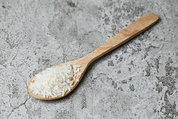 close up view of white raw rice on the wooden spoon. Grey or gray cement on the background.