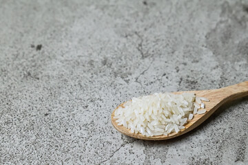 close up view of a half white raw rice on the wooden spoon. Grey or gray cement on the background. Copy space, empty, free, negative.