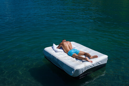 Nude man lying on a luxury mattress in sea water. Handsome man sunbathing by the lake or sea. Muscular sexy guy relaxing on a tropical beach. Hot sexy summer. Sexy tourist sunbathing.