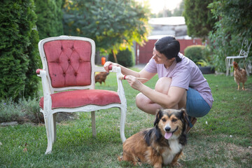 Woman painting a wooden furniture while sitting with her dog in the garden. DIY concept.