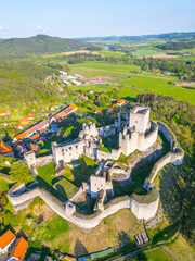 Aerial view showcases the historic Rabi Castle ruins surrounded by lush green fields and small village homes in Czechia. The structure reflects medieval architecture and rich history.