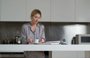 Woman eating breakfast in the modern kitchen in the morning. Portrait of a pretty woman with cup of coffee in cozy kitchen. Modern interior, furniture for the kitchen.