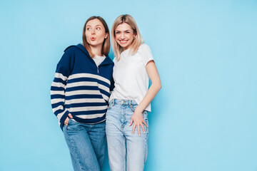Naklejka premium Two young beautiful smiling brunette hipster female in trendy summer clothes. Lovely women posing on blue background in studio. Positive models having fun. Cheerful and happy. isolated